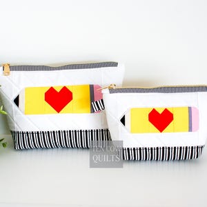Puede incluir: Dos estuches acolchados con forma de lápiz con cremallera y ribete de rayas blancas y negras. El estuche más grande tiene un lápiz amarillo con un corazón rojo y el estuche más pequeño tiene un lápiz amarillo con un corazón rojo. Los estuches están hechos por Ten-Cow Quilts.