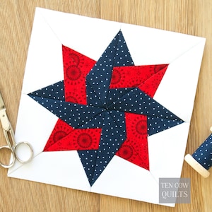 May include: A square quilt block featuring a central eight-pointed star pattern made of navy blue fabric with white triangles and red fabric with circular patterns, set against a white background with the text Ten Cow Quilts in the corner.