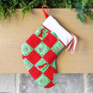 May include: A handmade Christmas stocking with a patchwork design of red polka dots and green squares. The stocking features festive patterns and a white cuff. Two candy canes are tucked inside. A red loop is attached for hanging.