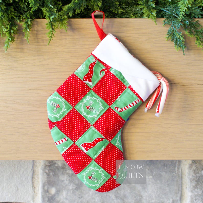 May include: A handmade Christmas stocking with a patchwork design of red polka dots and green squares. The stocking features festive patterns and a white cuff. Two candy canes are tucked inside. A red loop is attached for hanging.