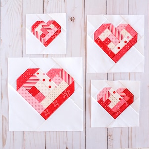 May include: Three white fabric squares with red and pink patchwork hearts in different sizes. The hearts are made of various patterned fabrics, including stripes, polka dots, and hearts.