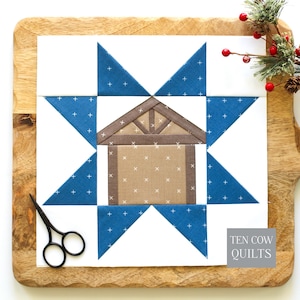 May include: A square quilt block featuring a central beige house with a brown roof, surrounded by a blue star pattern with white cross-stitch details on a white background. The text TEN COW QUILTS is visible in a gray box in the bottom corner.