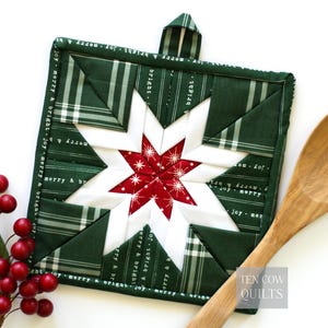May include: A square, quilted Christmas potholder with a star design. The star features a red center with white accents and is surrounded by green and white fabric. The border is green with white text that reads "joy merry & bright". A loop is attached for hanging.
