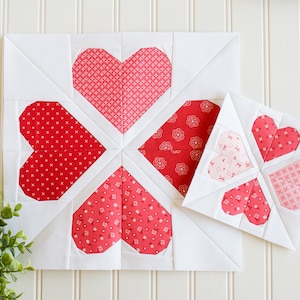Könnte beinhalten: Zwei weiße Stoffquadrate mit roten und rosa Herzen, die darauf genäht sind. Die Herzen bestehen aus verschiedenen gemusterten Stoffen. Das größere Quadrat hat vier Herzen und das kleinere Quadrat hat drei Herzen.