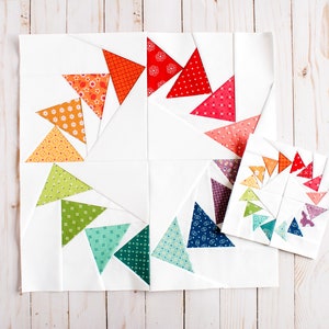 May include: Two quilt blocks with a spiral pattern of colourful fabric triangles. The larger block has a white background and the smaller block has a black background.