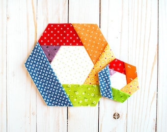 May include: Two colorful fabric hexagons, one larger than the other, are made of different patterned fabrics in shades of red, orange, yellow, green, blue, and white. The hexagons are made of multiple fabric pieces sewn together to create a geometric design.