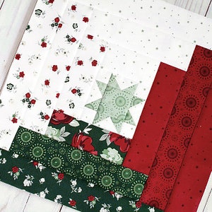 May include: A red, green and white patchwork quilt block with a star in the centre. The block is made up of different fabrics with various patterns, including floral, polka dot and geometric designs.