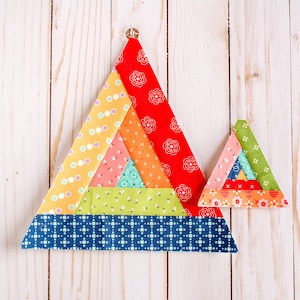 May include: Two colorful fabric triangles, one larger than the other, are made of multiple layers of different patterned fabrics. The larger triangle is blue, green, orange, pink, and red. The smaller triangle is green, blue, orange, and red. Both triangles are on a white wooden background.