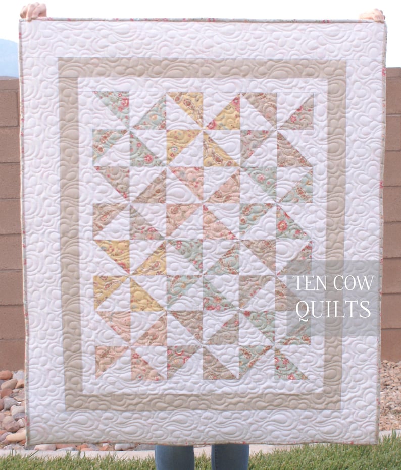 May include: A white quilt with a beige border and a pattern of pink, yellow, and green floral fabric triangles. The quilt is quilted with a wavy pattern. The text "TEN COW QUILTS" is in the bottom right corner.