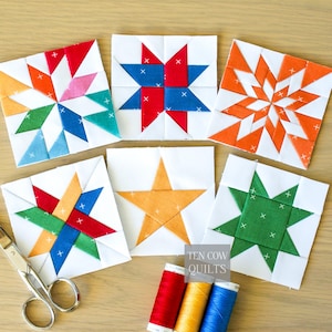Puede incluir: Una colección de bloques de edredón con forma de estrella coloridas sobre una superficie de madera. Cada bloque presenta un diseño de estrella único en tonos de rojo, azul, naranja, verde y amarillo. La imagen también incluye tijeras, carretes de hilo y el texto "TEN COW QUILTS".