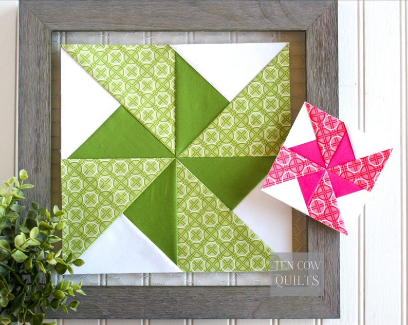 Pode incluir: Um bloco de colcha emoldurado com um design de cata-vento. O bloco apresenta tri&acirc;ngulos verdes e brancos, com um tecido verde estampado. Um cata-vento menor, separado, em rosa e branco fica ao lado. A moldura &eacute; cinza.