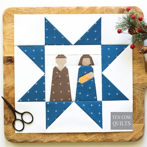 May include: A square quilt block featuring a central applique of two figures in brown and blue fabric, surrounded by a blue and white star pattern with a plus sign motif. The text TEN COW QUILTS is printed in a grey box in the bottom right corner.