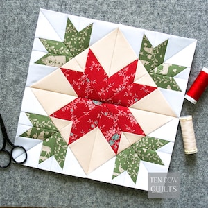 May include: A square quilt block featuring a central red floral star surrounded by cream-colored triangles and four green patterned corner motifs with deer and foliage prints. Black scissors and two spools of thread are nearby. Text reads TEN COW QUILTS.