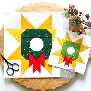 May include: Two square quilt blocks featuring a central green wreath with a red bow, surrounded by a yellow star on a white background. The blocks are displayed with black scissors. The text Ten Cow Quilts is visible in the bottom right corner.