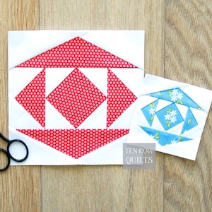 May include: Two fabric quilt blocks. The larger block features a red polka dot pattern within a white geometric design. The smaller block has a blue floral pattern. The text "TEN COW QUILTS" is visible.