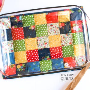 May include: A glass baking dish with a colourful patchwork fabric hot pad underneath. The fabric is made of squares in shades of red, yellow, green, blue, and white. The text "TEN COW QUILTS" is visible in the bottom right corner of the image.