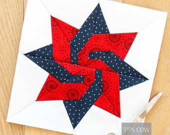 May include: A square quilt block featuring a star design in red and navy blue fabrics, set against a white background. The red fabric has a circular pattern, while the navy has white polka dots. The scissors are on the right side of the quilt block. The text "TEN COW QUILTS" is in the bottom right corner.