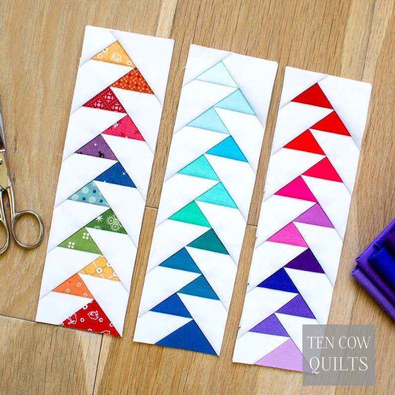 Puede incluir: Tres marcap&aacute;ginas de tela blanca con patrones triangulares coloridos. Cada marcap&aacute;ginas presenta una combinaci&oacute;n de colores diferente: rojo, naranja, amarillo, verde, azul y morado. El texto "TEN COW QUILTS" es visible en la esquina inferior derecha.