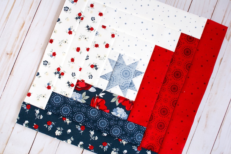 May include: A red, white and blue patchwork quilt block with a star design in the centre. The block is made up of different fabrics with floral, star and firework patterns.