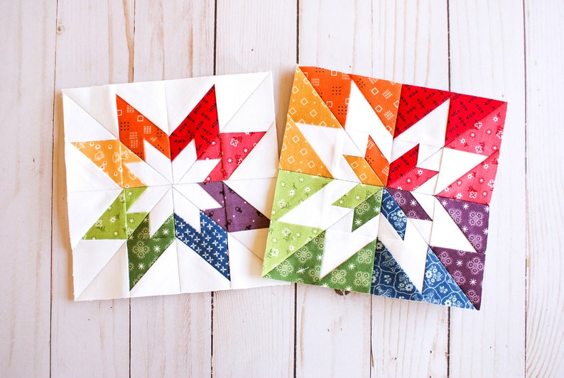 May include: Two colourful patchwork quilt blocks featuring a star design. The blocks are made with a variety of fabrics in shades of red, orange, yellow, green, blue, and purple. The blocks are sewn together with white fabric.