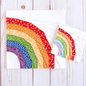 May include: Two fabric rainbow quilt blocks, one larger than the other, with a white background and colorful fabric strips sewn in a curved pattern to create a rainbow shape.