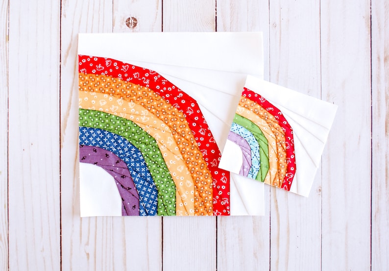 May include: Two fabric rainbow quilt blocks, one larger than the other, with a white background and colorful fabric strips sewn in a curved pattern to create a rainbow shape.