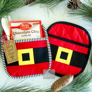 May include: A festive Christmas gift set with a red and black Santa-themed oven mitt and a matching pot holder. The pot holder has a pocket containing a Betty Crocker cookie mix, wooden spoons, and a tag saying "Making Spirits Bright."