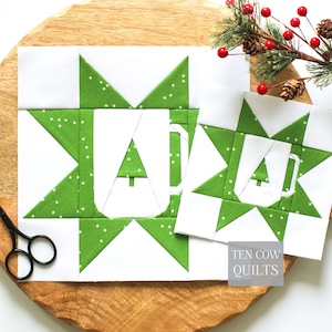 May include: Two square quilt blocks featuring a green star pattern with white speckles and a central white mug shape containing a small green tree. The blocks are white and green, with a small grey label reading TEN COW QUILTS.