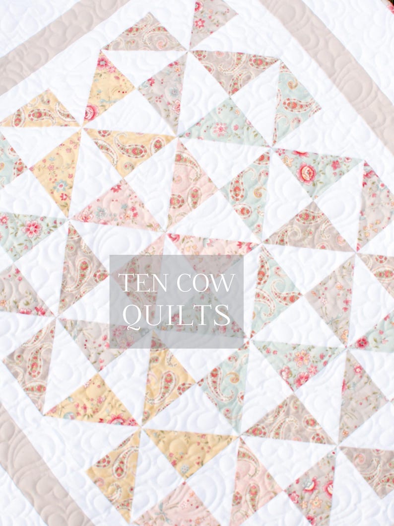 May include: A white quilt with a pattern of pastel pink, yellow, and blue triangles. The quilt is quilted with a swirl pattern. The text "TEN COW QUILTS" is in the center of the quilt.