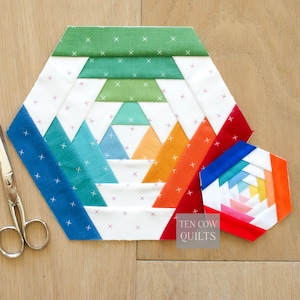 Pode incluir: Um bloco de colcha geométrico e colorido com um design de abacaxi. O bloco apresenta uma variedade de cores, incluindo azul, verde, laranja e vermelho, com detalhes brancos. Um bloco menor e concluído está ao lado do maior. O texto "TEN COW QUILTS" é visível.