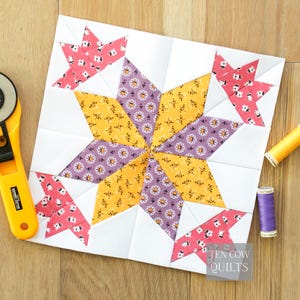 May include: A patchwork quilt block with a star design, incorporating white, yellow, purple, and pink floral fabrics. The block is displayed on a wooden surface, with a rotary cutter and thread spools. The text "TEN COW QUILTS" is visible.