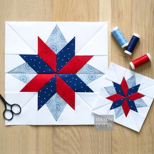 Peut inclure: Deux blocs de courtepointe en tissu blanc avec des motifs d'étoiles rouges et bleues. Le plus grand bloc mesure environ 30 cm de côté, et le plus petit bloc mesure environ 15 cm de côté. Trois bobines de fil et une paire de ciseaux sont également visibles.