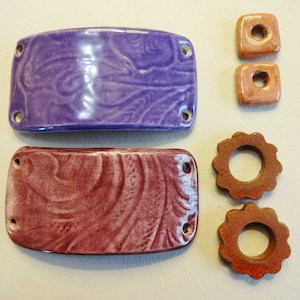 May include: Two ceramic rectangular tiles with a swirled pattern, one purple and one maroon, and four ceramic round tiles with a hole in the center, two orange and two brown.