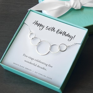 May include: A sterling silver necklace featuring five interlocking circular rings of varying sizes, presented in a light blue gift box. The card inside reads Happy 50th Birthday! Five rings celebrating five wonderful decades. Maggie Blake Jewelry 925 Sterling Silver.