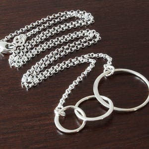May include: A silver chain necklace with three interlocking circles as a pendant.