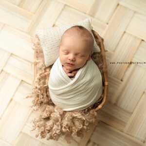 May include: A newborn baby is swaddled in a white blanket and sleeping in a woven basket lined with a fluffy brown material. The baby is lying on a white pillow with a delicate pattern.