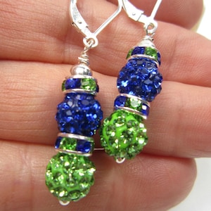 May include: Dangle earrings with a lever back closure. Each earring features a combination of green and blue crystal beads. The earrings have a silver-tone metal finish and are designed to be eye-catching.