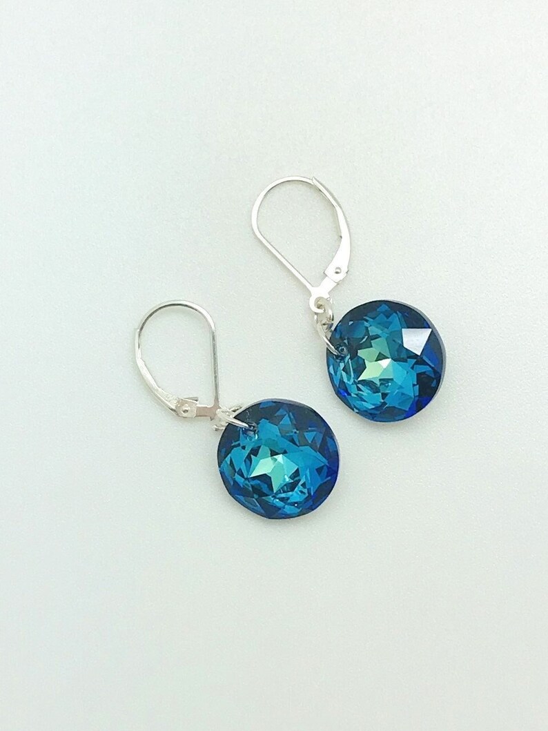 May include: A pair of silver dangle earrings with blue crystal stones. The stones are round and have a faceted design.