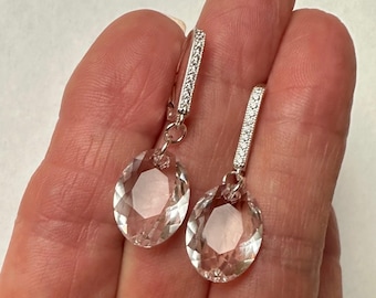 May include: A pair of silver dangle earrings with clear crystal teardrop-shaped stones. The earrings have a silver bar with small clear stones.