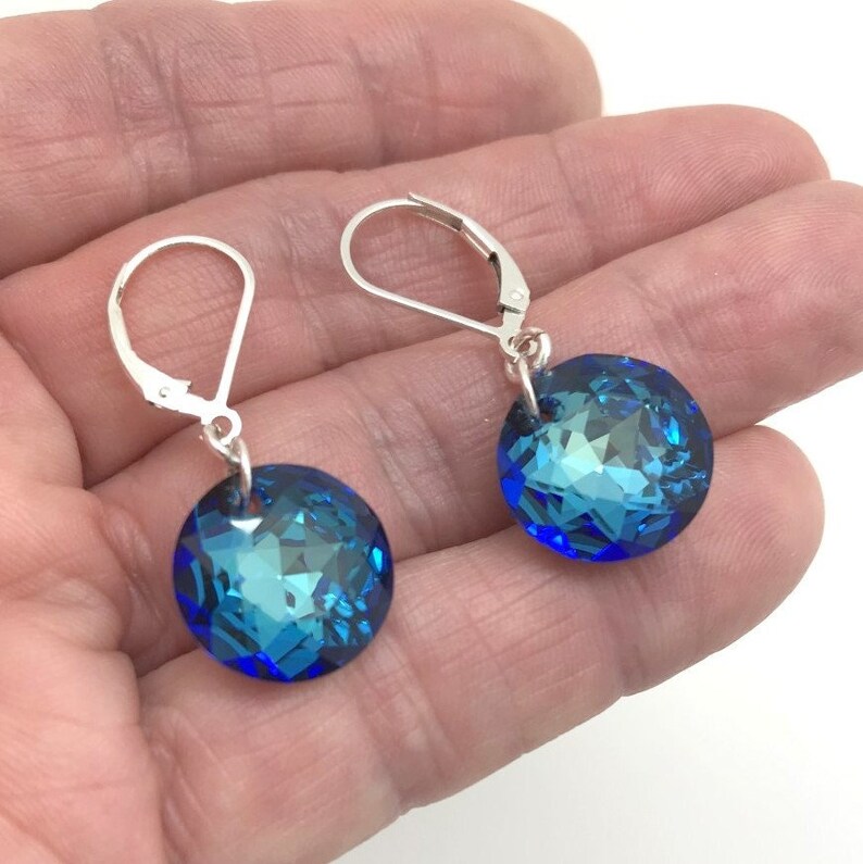 May include: A pair of silver dangle earrings with blue crystal round stones. The earrings have lever back closures.