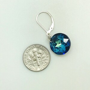 May include: A pair of silver earrings with a blue crystal gemstone. The crystal is faceted and has a round shape. The earrings are approximately the size of a ten pence piece.