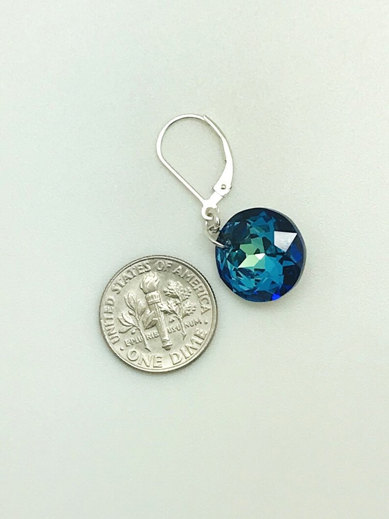 May include: A pair of silver earrings with a blue crystal gemstone. The crystal is faceted and has a round shape. The earrings are approximately the size of a ten pence piece.