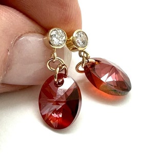May include: A pair of gold earrings with a small clear crystal at the top and a larger red crystal dangling below.
