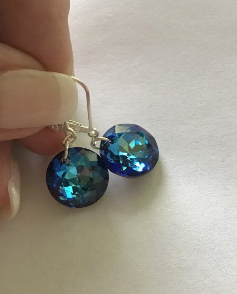 May include: A pair of silver dangle earrings with blue crystal stones. The stones are faceted and have a shimmery finish.