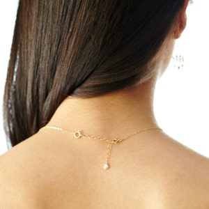 May include: A gold chain necklace with a small pearl pendant. The necklace is worn by a person with long dark hair.