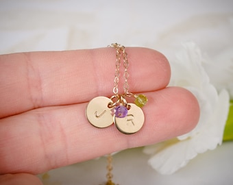 May include: Gold necklace with two small round charms, one with the letter 'J' and the other with the letter 'R'. The charms are attached to a delicate gold chain and have small purple and green gemstones.