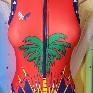 May include: Red sleeveless bodysuit with a zipper down the front. The bodysuit features a palm tree and a stylized design of a flag with yellow, red, and blue colors.