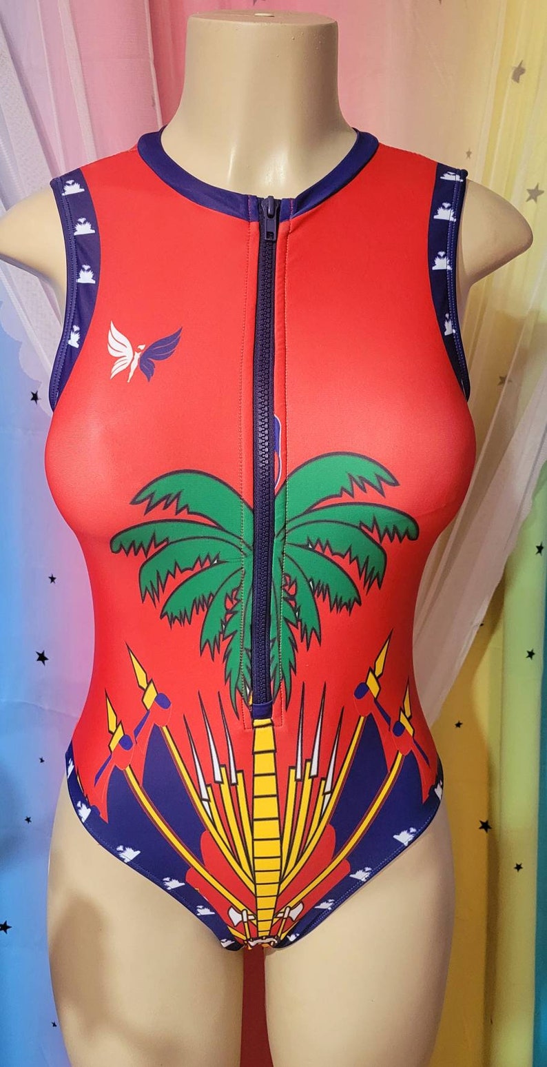 May include: Red sleeveless bodysuit with a zipper down the front. The bodysuit features a palm tree and a stylized design of a flag with yellow, red, and blue colors.