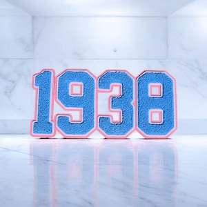 May include: A decorative sign featuring the year "1938" in a bold, collegiate-style font. The numbers are blue with a pink border, set against a white marble background. The sign's reflection is visible on the surface.