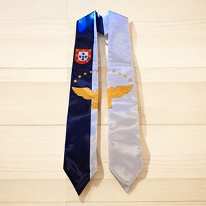 May include: A blue and white graduation sash with a gold eagle and the Portuguese coat of arms.